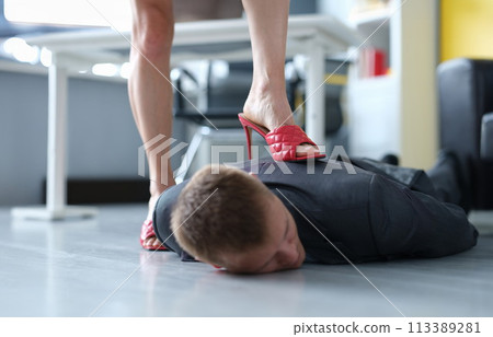 Woman in red heeled sandals stands on back of lying man Woman in red heeled sandals stands on back of lying man 113389281