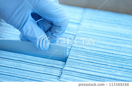 Gloved hand of doctor pulls out disposable blue medical napkin closeup 113389288
