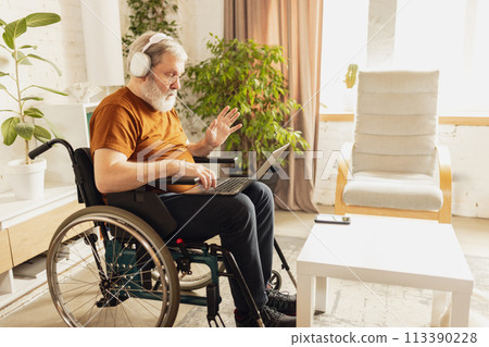 Elderly man sitting in headphones and having online video call via laptop with colleagues. Businessman working remotely at home 113390228