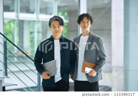 Two business people standing with laptops in office aisle 113390317
