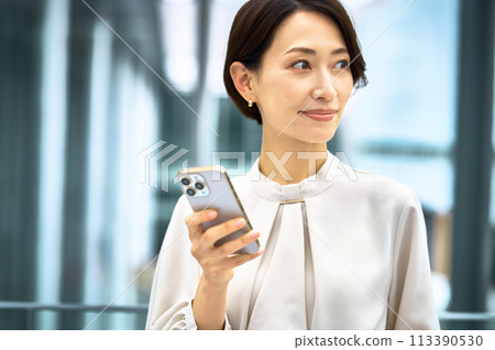 穿著商務休閒服的中層女商人在辦公室走廊裡看智能手機 穿著商務休閒服的中層女商人在辦公室走廊裡看智能手機 113390530