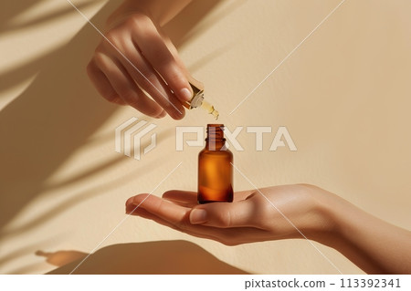 Two hands gently holding an amber dropper bottle with blank label mockup, on a beige background. Beauty product fluid oil advertising. Close up oily pipette pump packaging template. Skincare design Two hands gently holding an amber dropper bottle with blank label mockup, on a beige background. Beauty product fluid oil advertising. Close up oily pipette pump packaging template. Skincare design 113392341