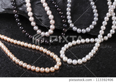 Collection of pearl necklaces placed on black rocks with black background 113392406
