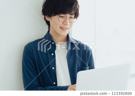 A young man wearing glasses operating a computer 113392600
