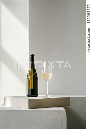 A bottle of white wine and a wine glass are on a white surface A bottle of white wine and a wine glass are on a white surface 113393875