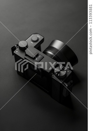 A black camera with a black lens sits on a black surface 113393881