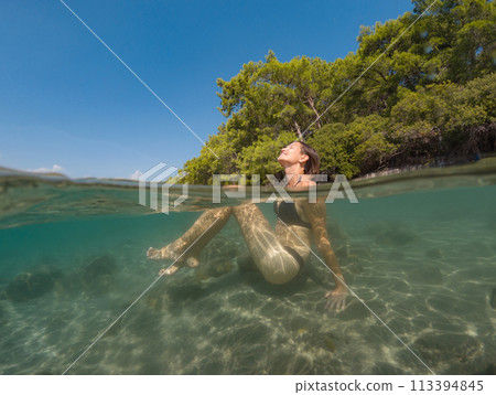 Young female on holidays enjoy floating on a crystal clear water beach of Antalya Turkey. Asian beautiful woman swimming with open arms. Relax and tranquility. Travel and Holiday concept. 113394845