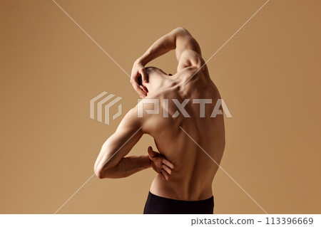 Rear view of bald man with muscular build body stretching his neck, highlighting strong physique against beige studio background. Rear view of bald man with muscular build body stretching his neck, highlighting strong physique against beige studio background. 113396669