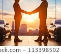 Silhouetted handshake between car salesman and buyer at sunset with new cars in background 113398502