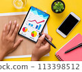 Overhead view of hands reviewing colorful growth charts on a digital tablet 113398512