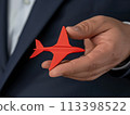 Businessman's hand holding a small red airplane, representing business travel and aviation industry themes in a close-up shot 113398522