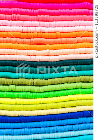 A vibrant collection of clay beads, neatly arranged by color on a white table, ready to inspire young crafters to create their own unique bracelets. A vibrant collection of clay beads, neatly arranged by color on a white table, ready to inspire young crafters to create their own unique bracelets. 113398729