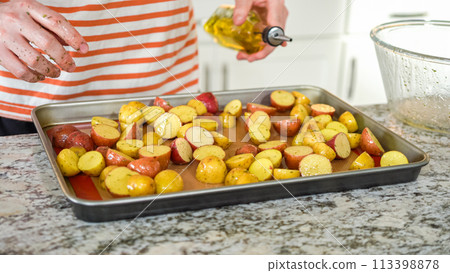 In a modern, white kitchen, a young man is engrossed in dinner preparations. His current endeavor includes arranging seasoned rainbow potatoes on a baking sheet, a meticulous step towards a In a modern, white kitchen, a young man is engrossed in dinner preparations. His current endeavor includes arranging seasoned rainbow potatoes on a baking sheet, a meticulous step towards a 113398878