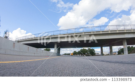 On a clear winter day, a car smoothly travels along Highway 101 near Santa Maria, California, under a brilliant blue sky, surrounded by a blend of greenery and golden hues. 113398973