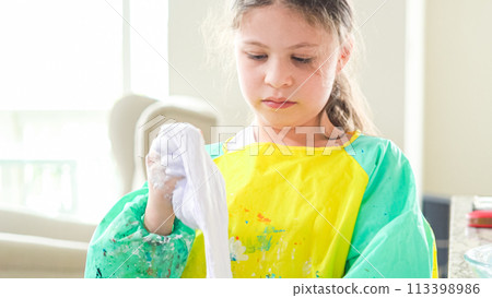 In a modern kitchen, a homeschooled girl is engrossed in creating homemade slime, a fun and educational hands-on project that enhances her creativity and problem-solving skills. 113398986