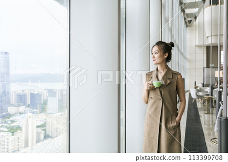 asian woman standing by window looking at view asian woman standing by window looking at view 113399708