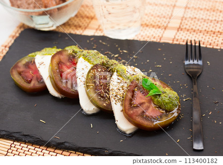 Caprese salad with mozzarella, black tomatoes and pesto on black stone plate Caprese salad with mozzarella, black tomatoes and pesto on black stone plate 113400182