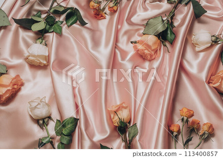 Simple beautiful roses flowers on satin fabric background. Gentle pink pearl cream waves folder satin fabric, with hammers of light, the surface, flat lay back up copy space for product or text 113400857