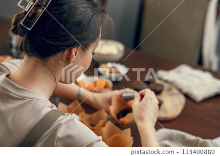 A young woman makes indentations in cupcakes for filling. the concept of baking at home in the kitchen for a birthday. copy space 113400880