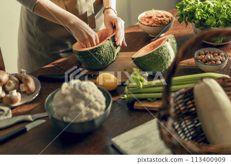 A young woman cleans a pumpkin with a knife for baking in an apron in the kitchen. The concept of healthy eating A young woman cleans a pumpkin with a knife for baking in an apron in the kitchen. The concept of healthy eating 113400909