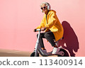 Smiling happy cool gray haired old senior woman on scooter moves on pink background. Older people freedom spirit concept 113400914