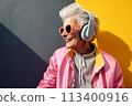 An elderly woman in sunglasses listens to music with headphones outdoors 113400916