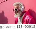 An elderly man in sunglasses listens to music with headphones outdoors 113400918