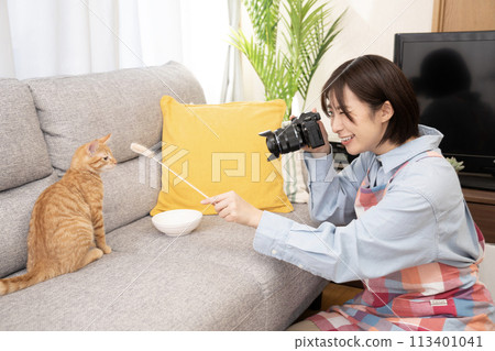 A woman taking a photo of a kitten with a cat toy 113401041