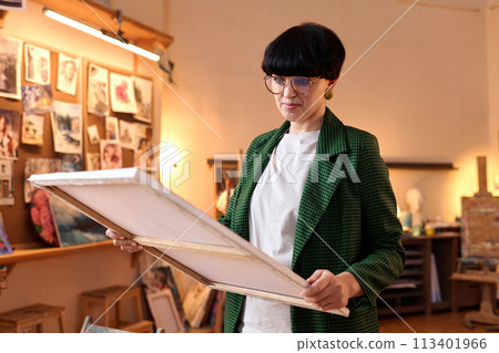 Waist up portrait of female artist holding oil painting on canvas in workshop, copy space 113401966
