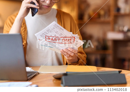 Close up of unrecognizable woman holding past due bill and calling on phone, copy space Close up of unrecognizable woman holding past due bill and calling on phone, copy space 113402018