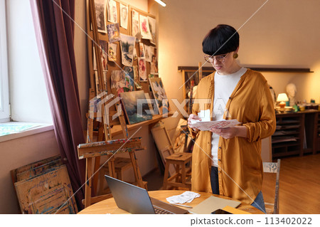 Waist up portrait of female business owner sorting bills and taxes while managing finances in art studio, copy space Waist up portrait of female business owner sorting bills and taxes while managing finances in art studio, copy space 113402022