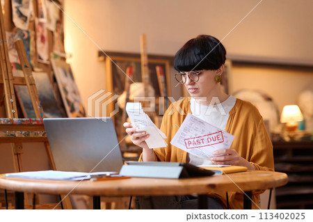 Portrait of female artist sorting bills and taxes while managing small business Portrait of female artist sorting bills and taxes while managing small business 113402025
