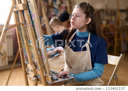 Side view portrait of young girl with disability enjoying art class in studio and painting on canvas Side view portrait of young girl with disability enjoying art class in studio and painting on canvas 113402137