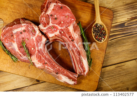 Raw fresh beef rib eye steaks on bone with spices and rosemary on wooden table. Top view 113402577