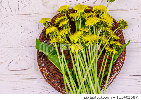 Yellow dandelion flowers in wicker basket on white wooden background. Top view 113402587