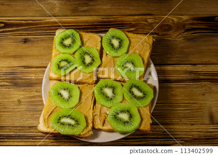 Tasty sandwiches with peanut butter and kiwi fruits on wooden table. Top view 113402599