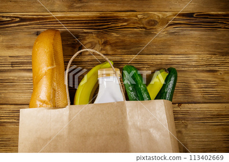 Paper bag with different food on wooden table. Top view. Grocery shopping concept Paper bag with different food on wooden table. Top view. Grocery shopping concept 113402669