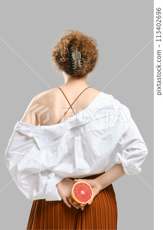 The woman turned away and holds half a grapefruit in her hands behind her back. 113402696