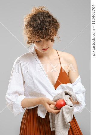 Woman wiping an apple with a towel over grey background Woman wiping an apple with a towel over grey background 113402704