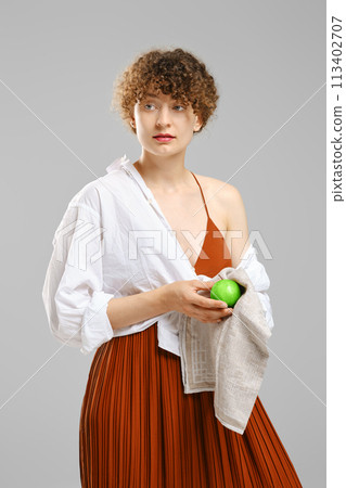 Woman wiping an apple with a towel and looking to the side Woman wiping an apple with a towel and looking to the side 113402707