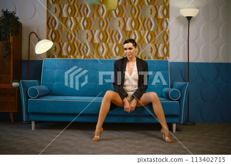 Fashionable woman in knitted body suit and oversized jacket sitting on vintage sofa 113402715
