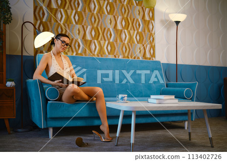 Woman sits on a vintage blue sofa in a old-fashioned living room and reading the book Woman sits on a vintage blue sofa in a old-fashioned living room and reading the book 113402726