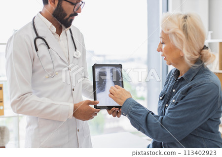Skilled radiologist in white uniform explaining visible changes on x-ray image. 113402923