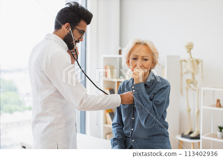 Serious old woman coughing while visiting family doctor for full examination. Serious old woman coughing while visiting family doctor for full examination. 113402936