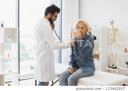 Bearded man in white lab coat checking lungs and heart via stethoscope. 113402937