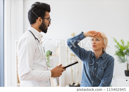 Respected man doctor and senior woman patient sitting at exam couch. Respected man doctor and senior woman patient sitting at exam couch. 113402945