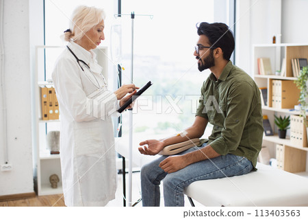 Bearded man receiving chemotherapy looking at nurse with tablet. 113403563