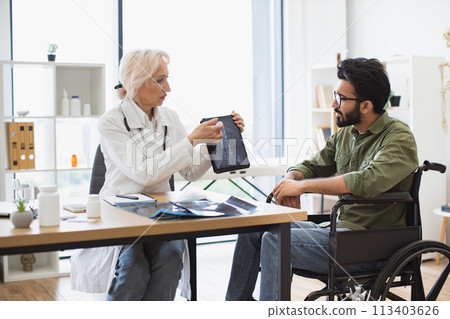 Senior specialist discussing results of diagnostic tests with wheelchair user. 113403626