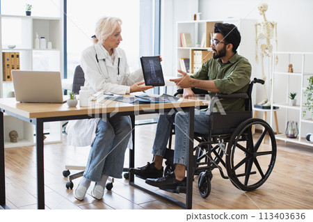 Senior lady demonstrating spine scans on tablet to mindful man using wheelchair Senior lady demonstrating spine scans on tablet to mindful man using wheelchair 113403636