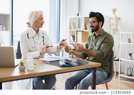 Senior female general practitioner communicating with young patient. 113403648